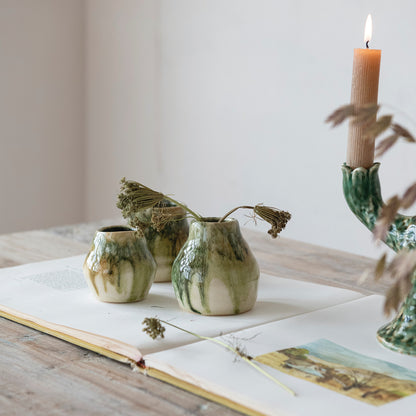Three ceramic vases on an open book with a candle and dried plants in the background.