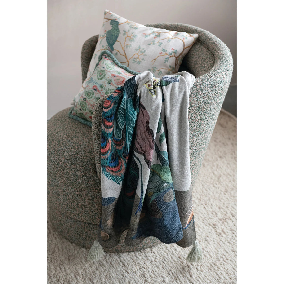 peacock throw blanket draped over an armchair with 2 decorative pillows on it