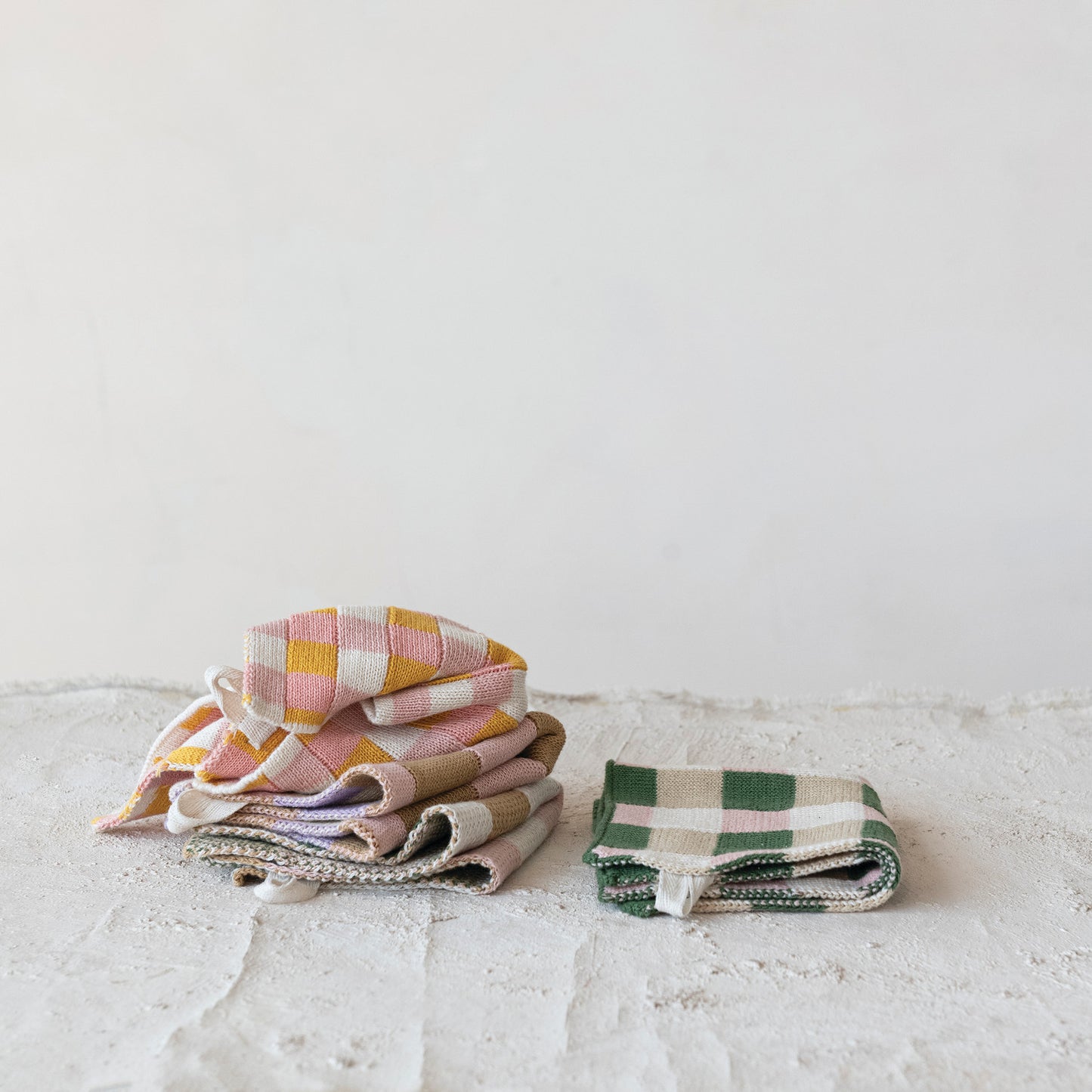 Stack of folded checkered dishcloths on a light plaster surface with a white background