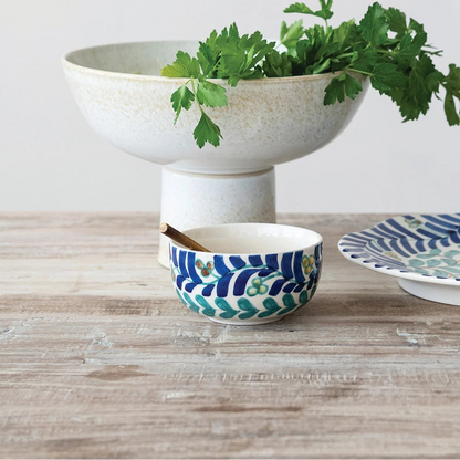 Ceramic bowls and a platter with greenery on a wooden surface
