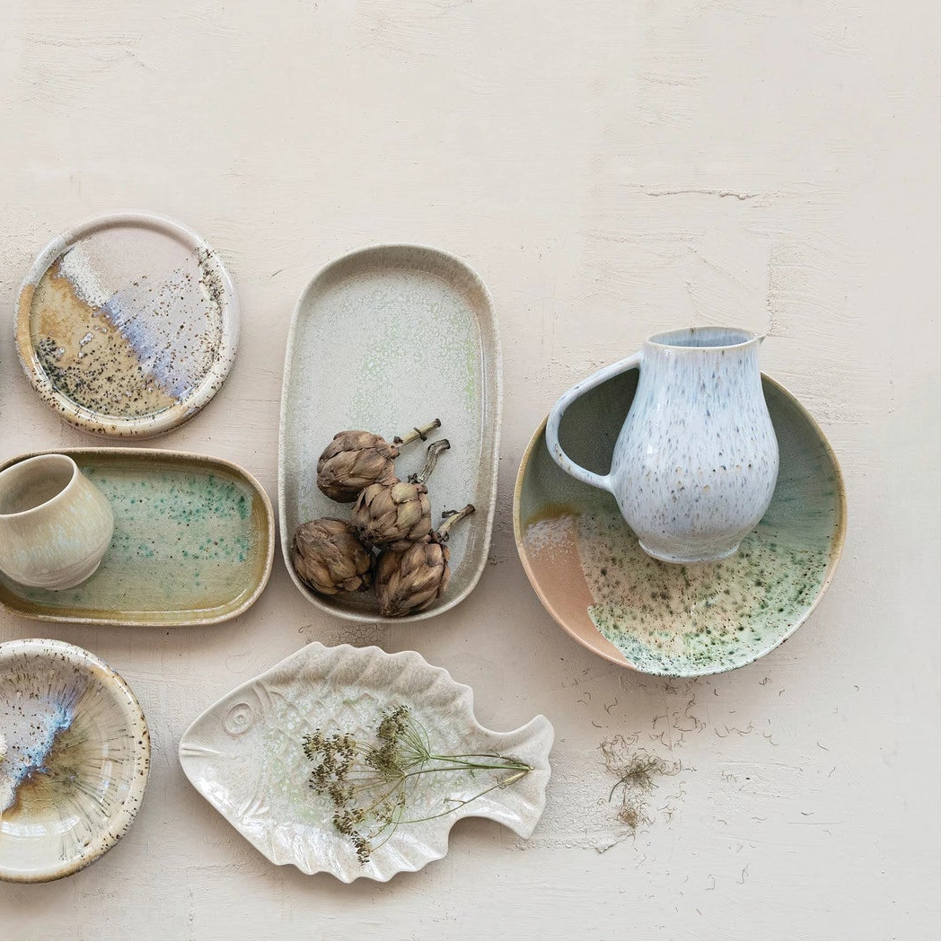 Collection of ceramic dishes and cups with reactive glaze designs arranged on a light background