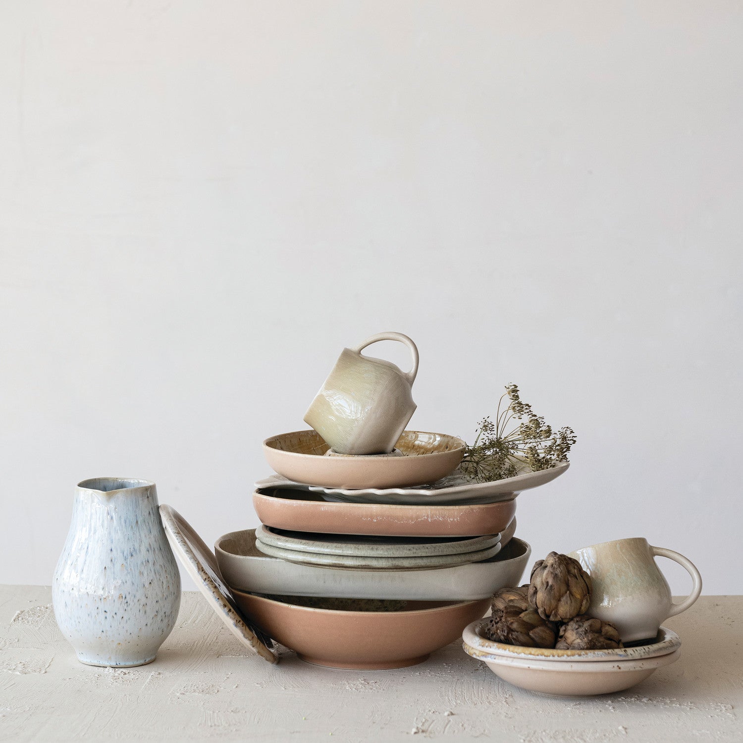 Stack of ceramic bowls and mugs on a white surface with a light gray background