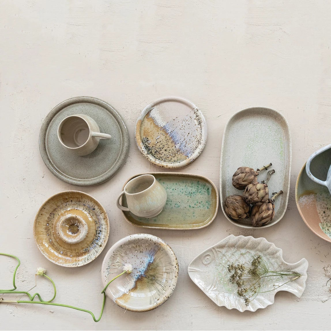 Collection of ceramic dishes and cups with reactive glaze designs arranged on a light background