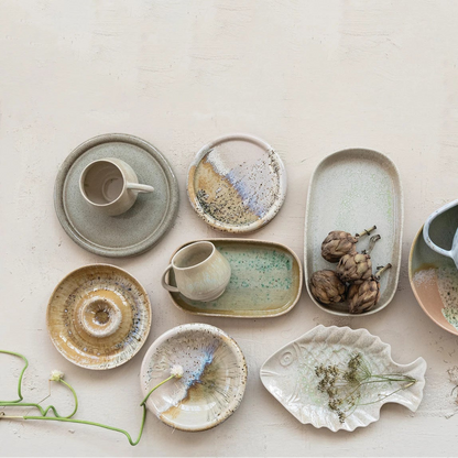 Collection of ceramic dishes and cups with reactive glaze designs arranged on a light background