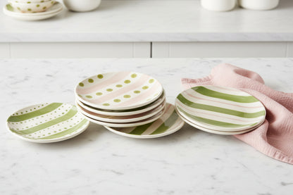 assorted small round plates with pink and green dots and stripes stacked on a countertop with a pink dishtowel