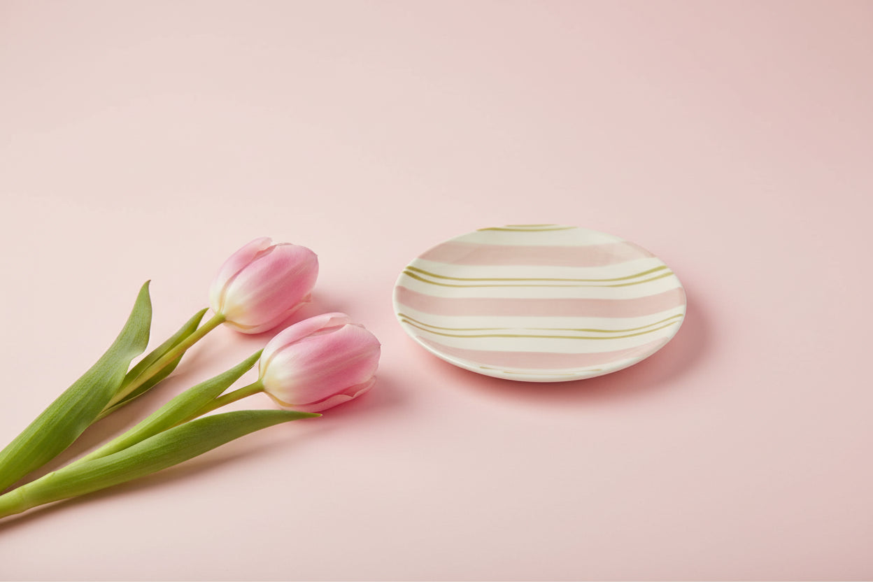 small round plate with pink and green stripes on a light pink background with  pink tulips