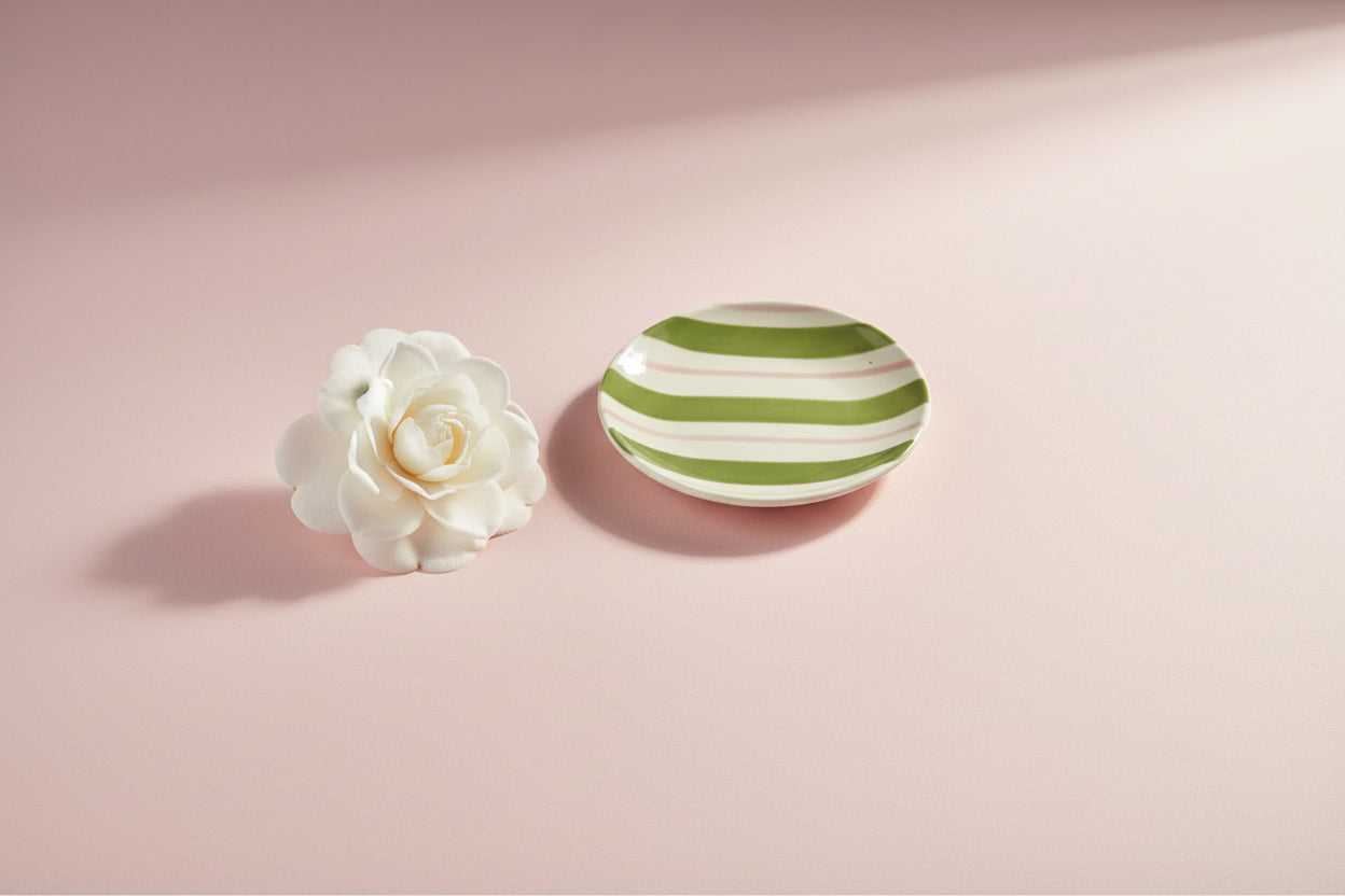 small round plate with pink and green stripes  on a light pink background with a white flower