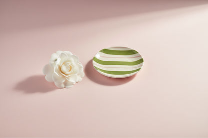 small round plate with pink and green stripes  on a light pink background with a white flower