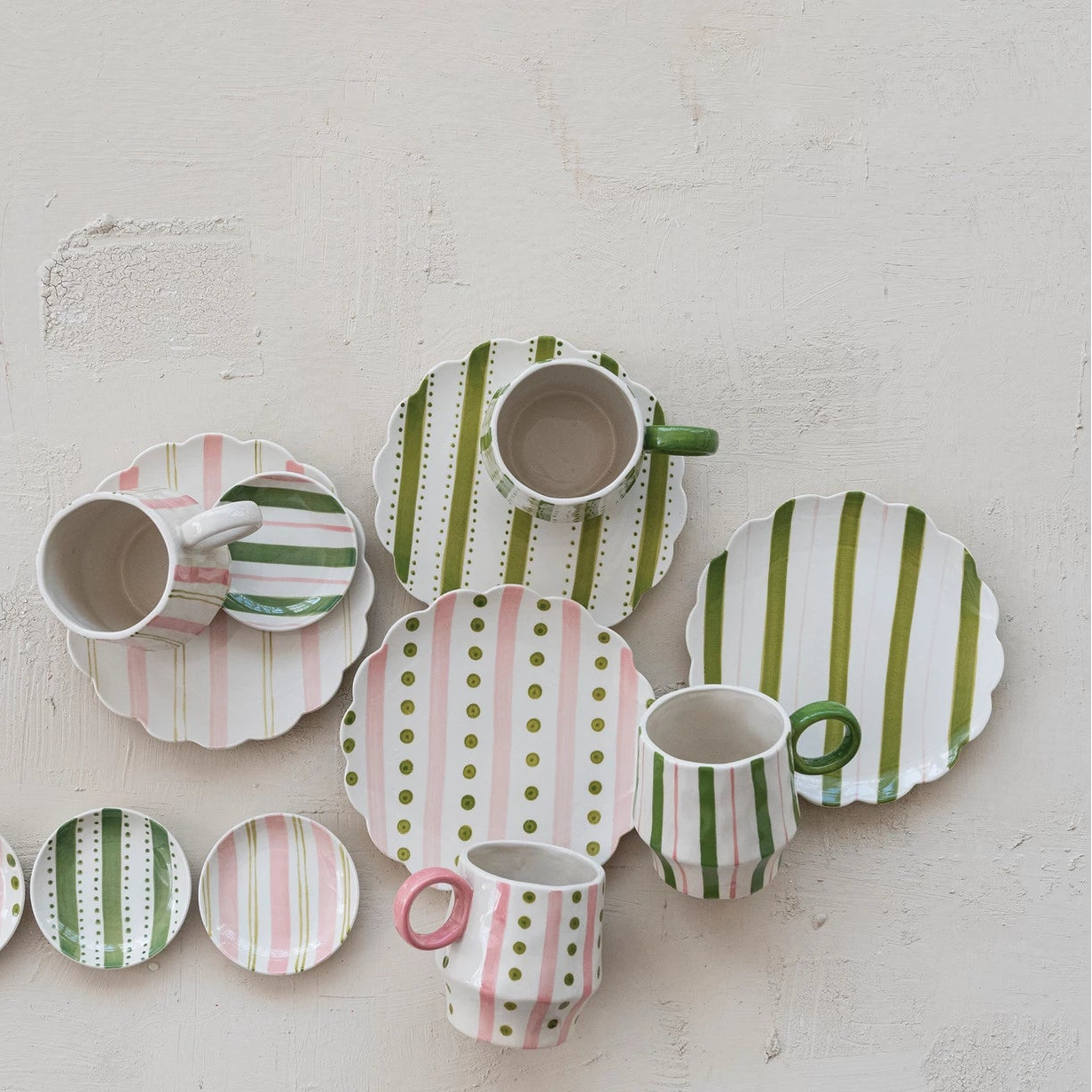 ceramic plates and mugs with pink and green striped and polka dot patterns on a plaster surface