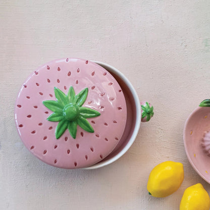 top view of a pink Strawberry Shaped Baker with lid set askew set on a plaster surface