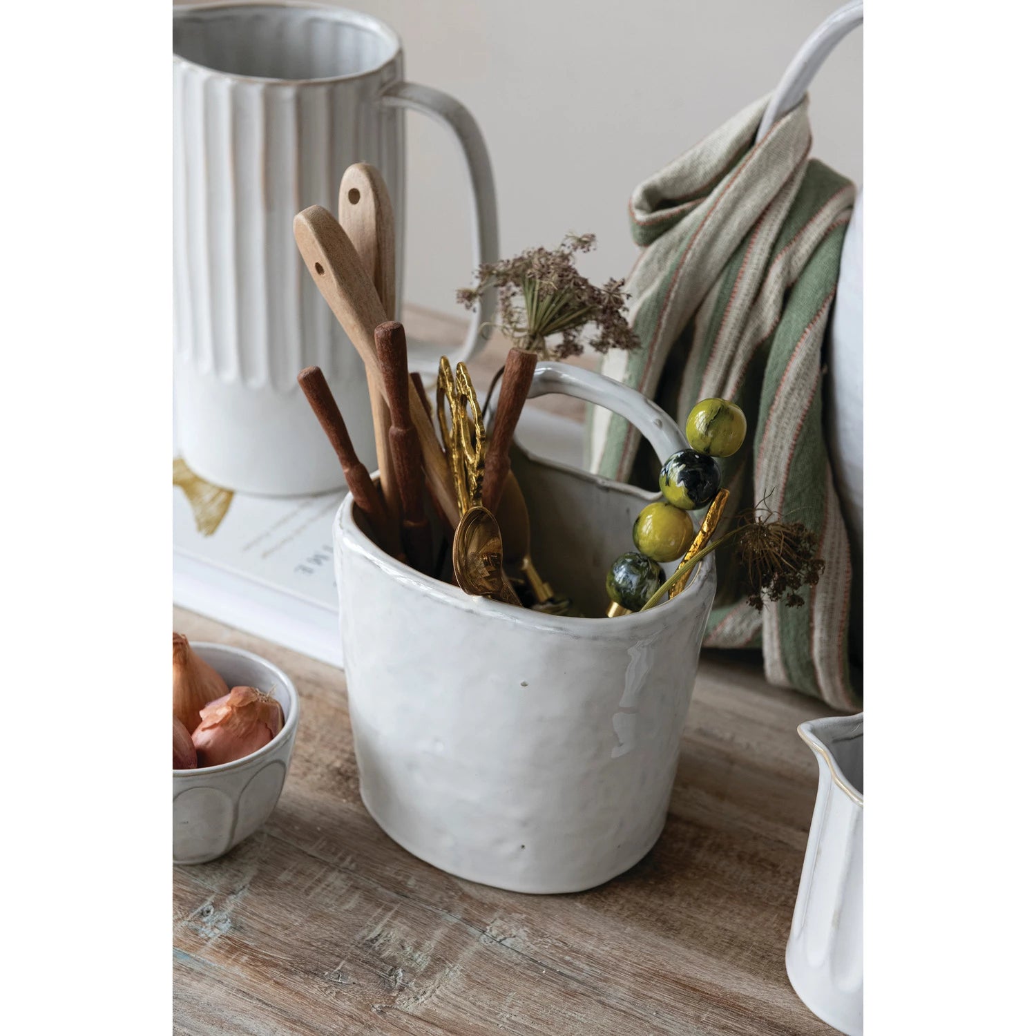White ceramic container with wooden utensils and dried plants on a wooden surface