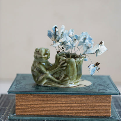 Ceramic frog vase with flowers on a textured surface