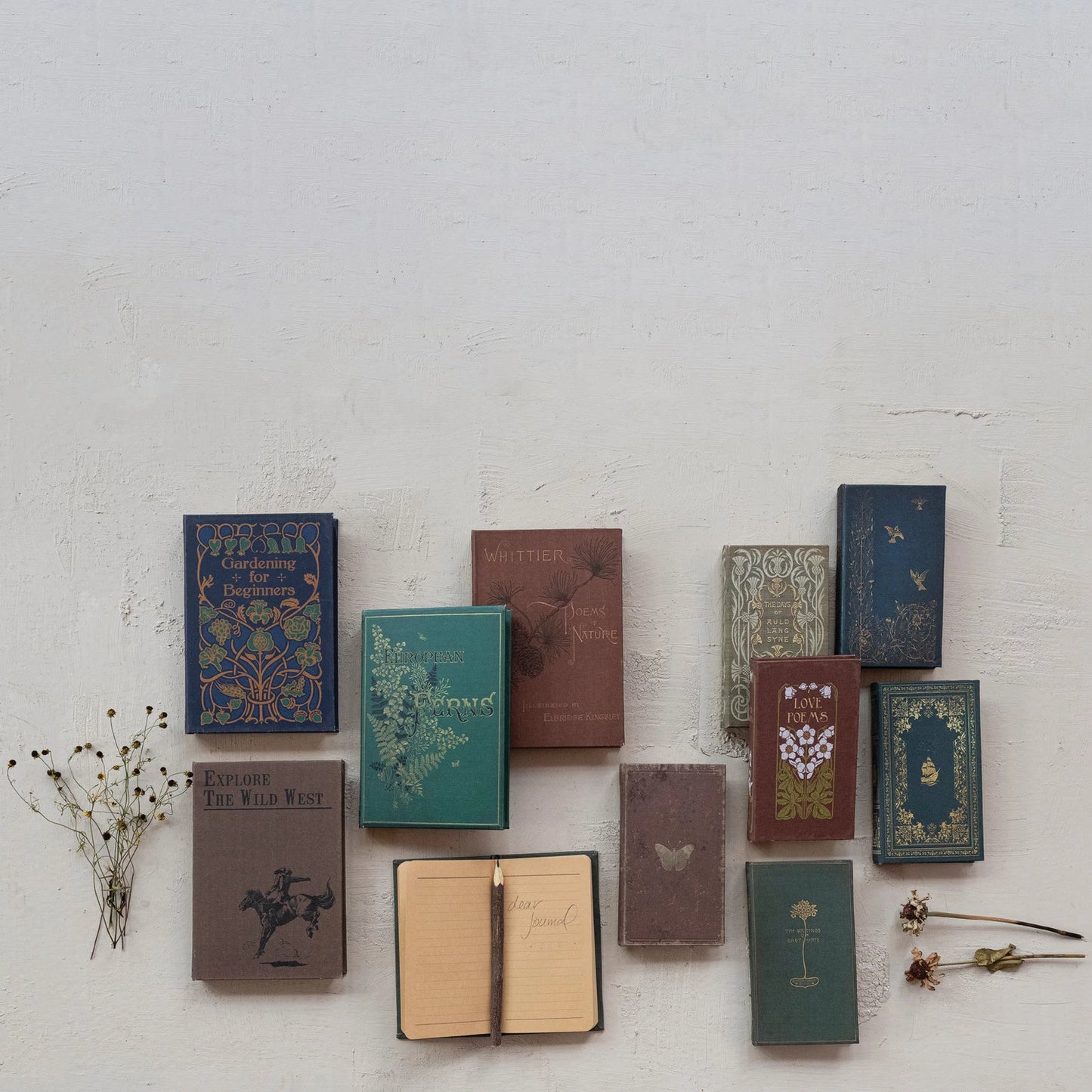 assorted books, one open showing lined pages with a pencil set on it arranged on a grey surface with dried botanicals