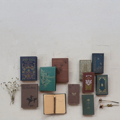 assorted books, one open showing lined pages with a pencil set on it arranged on a grey surface with dried botanicals