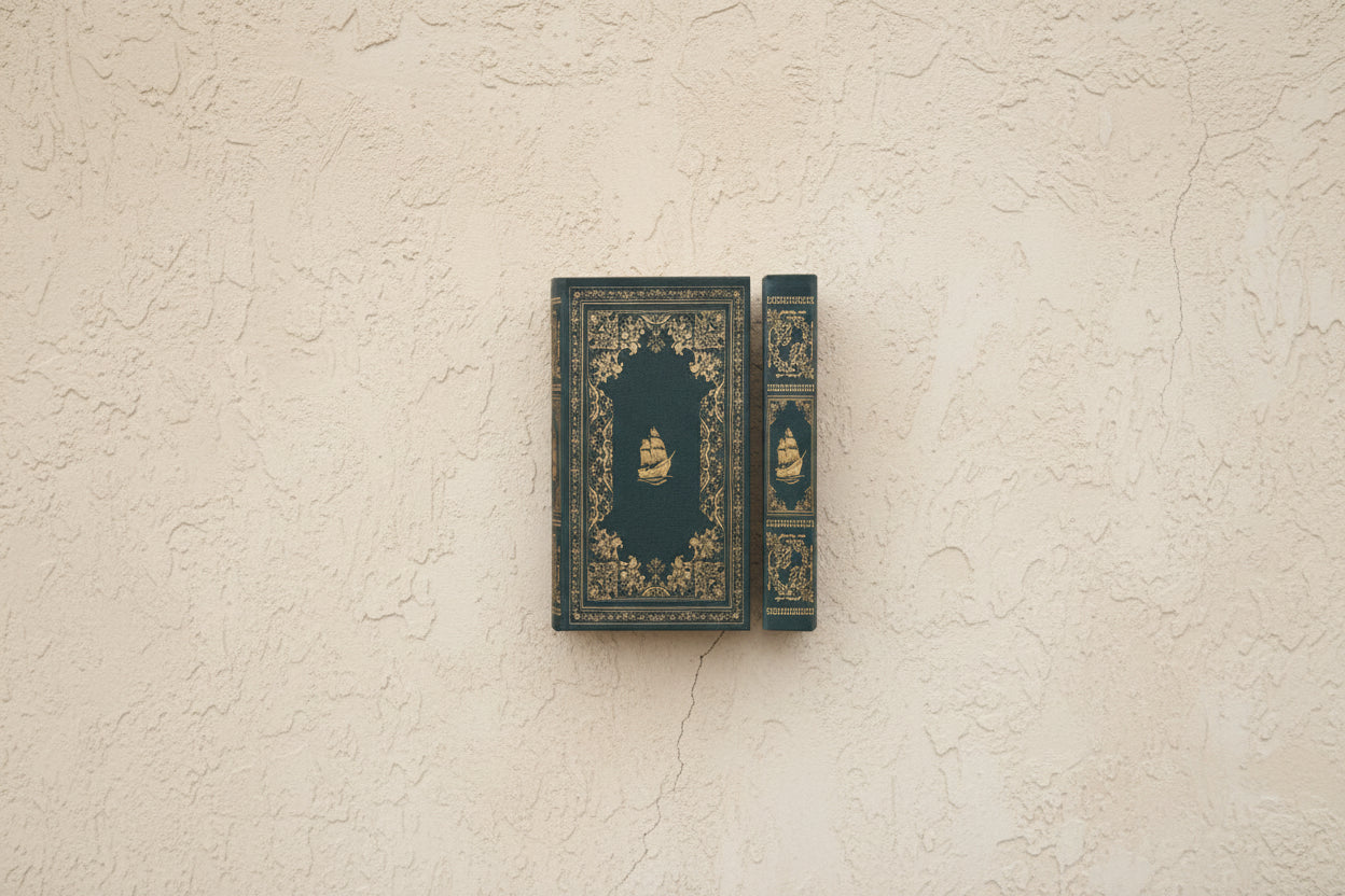 vintage style blue-green book cover and spine with ornate gold design and ship image in the center shown on a beige plaster surface