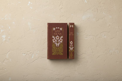 burgundy vintage style book with white floral design and titled " love poems" shown on a beige plaster surface