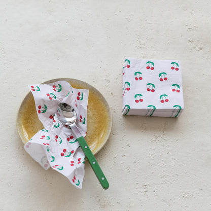 Napkin with cherry pattern on a plate with a spoon and a stack of cherry napkins next to it