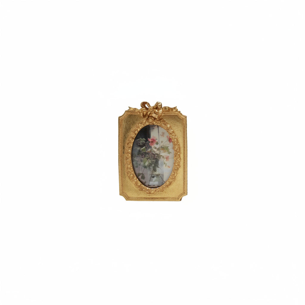 golden frame with bow on top and floral image in oval opening