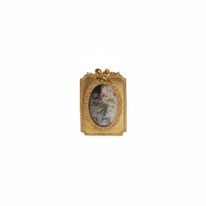 golden frame with bow on top and floral image in oval opening