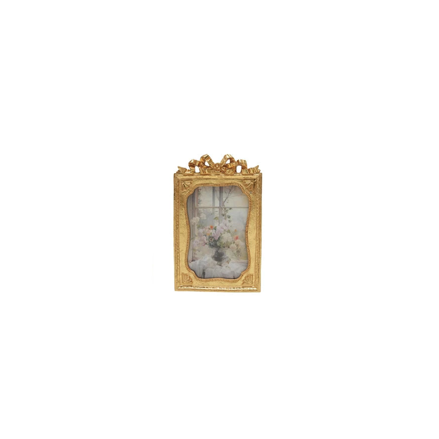 golden frame with bow on top and still life image in scrolled opening