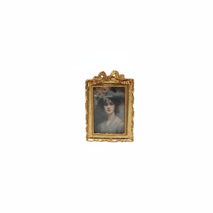 golden frame with bow on top and portrait of a woman in rectangular opening