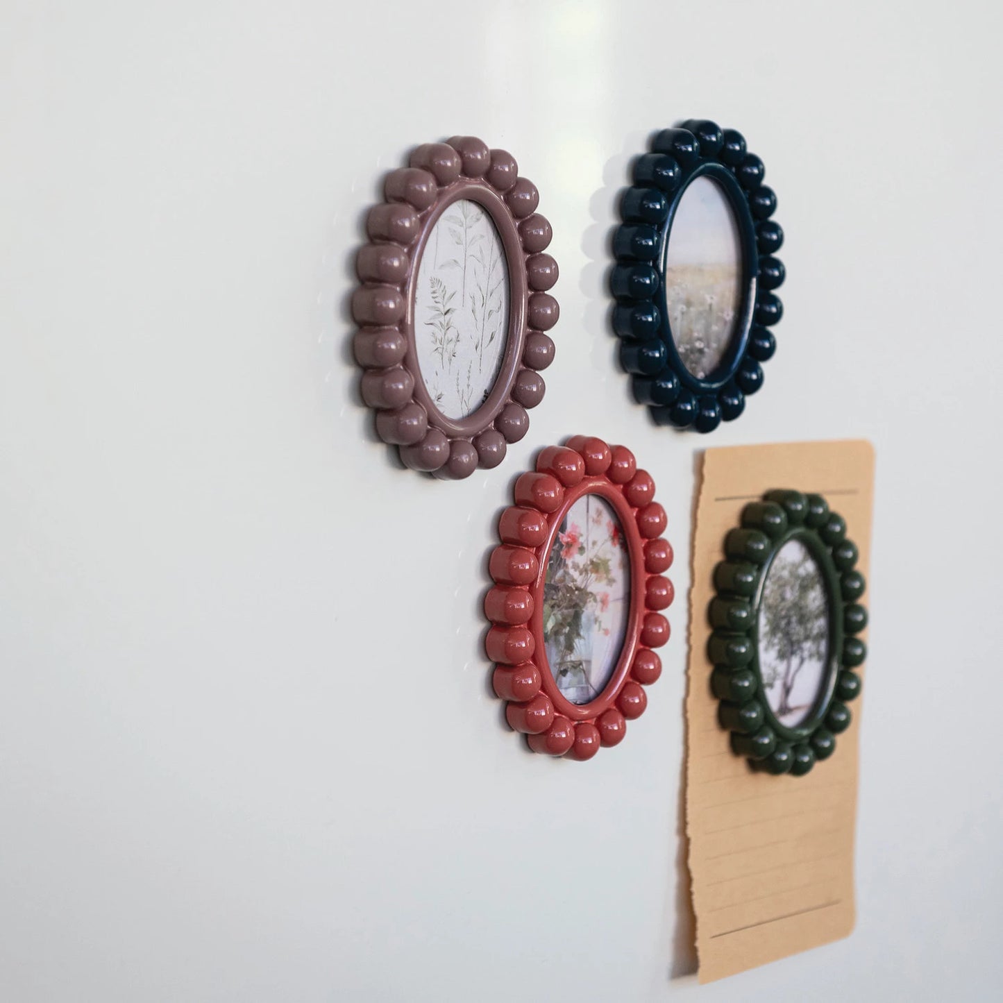 Four decorative frames in different colors on a white magnetic surface, one has a piece of paper under it