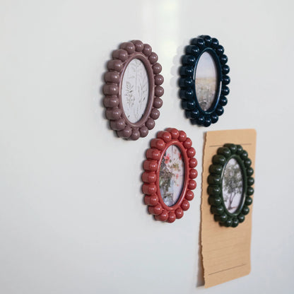 Four decorative frames in different colors on a white magnetic surface, one has a piece of paper under it