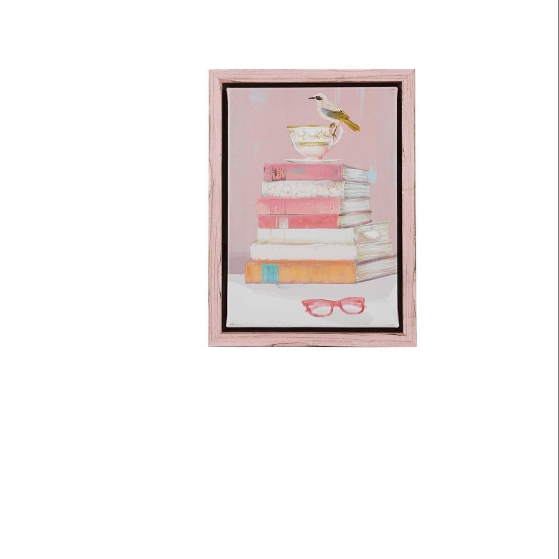 pink framed art print featuring a stack of pink and cream books with a bird perched on a teacup on top set against a light pink background with red-rimmed glasses at the bottom.