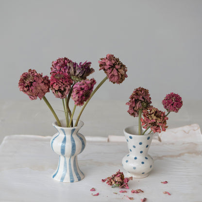 2 small bud vases with blue dots or stripes on them and dried flowers in them set on a white cloth