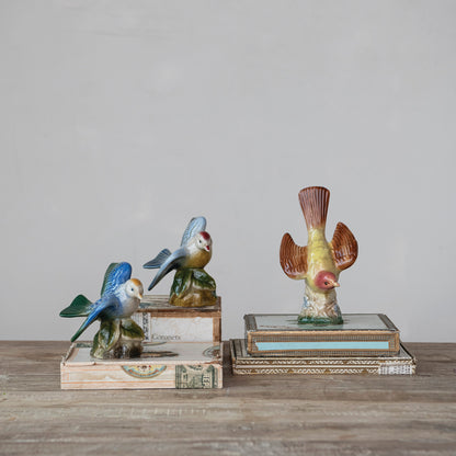 decorative ceramic bird figures arranged on books on a wooden table