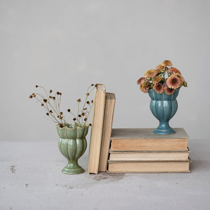 1 green and 1 blue ruffled small vase arranged with books and filled with flowers on a table