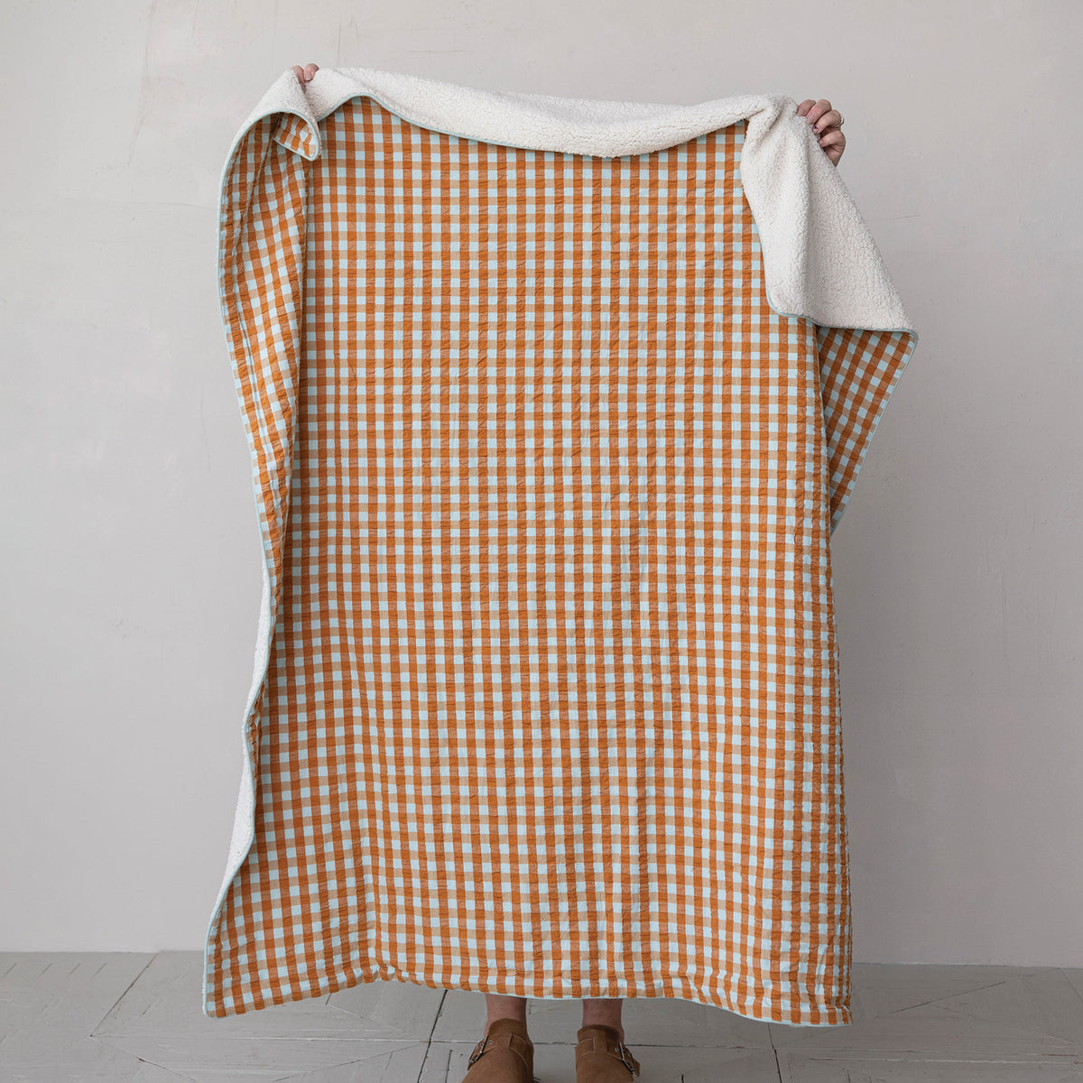 orange and light blue gingham throw blanket being held by a person standing behind it