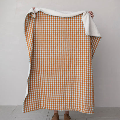 orange and light blue gingham throw blanket being held by a person standing behind it