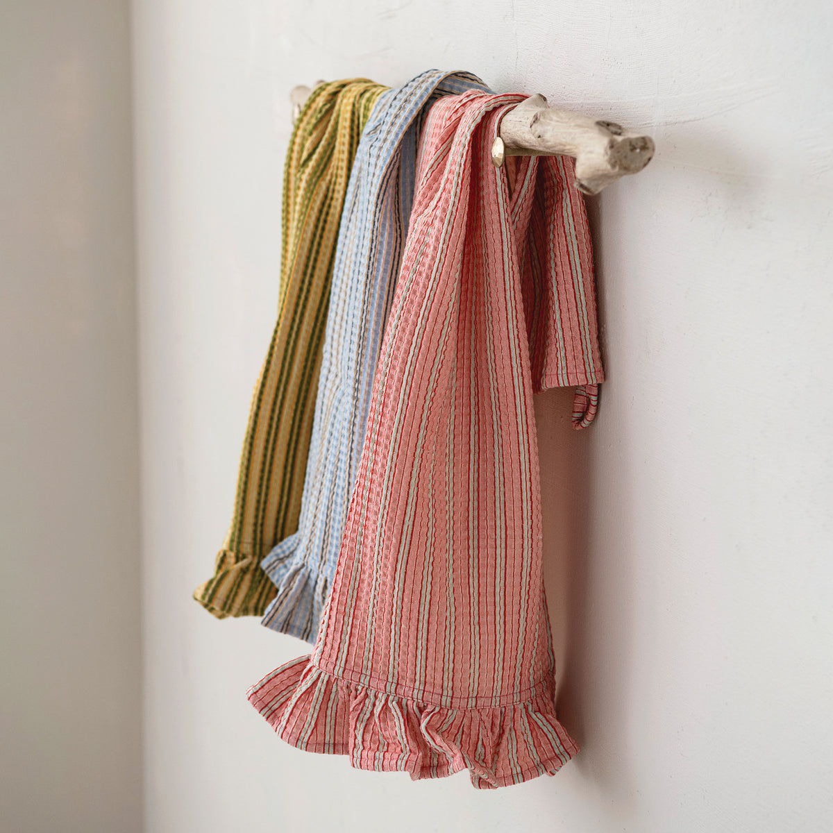 side view of 3 assorted striped tea towels hanging on a natural wood branch against a white wall