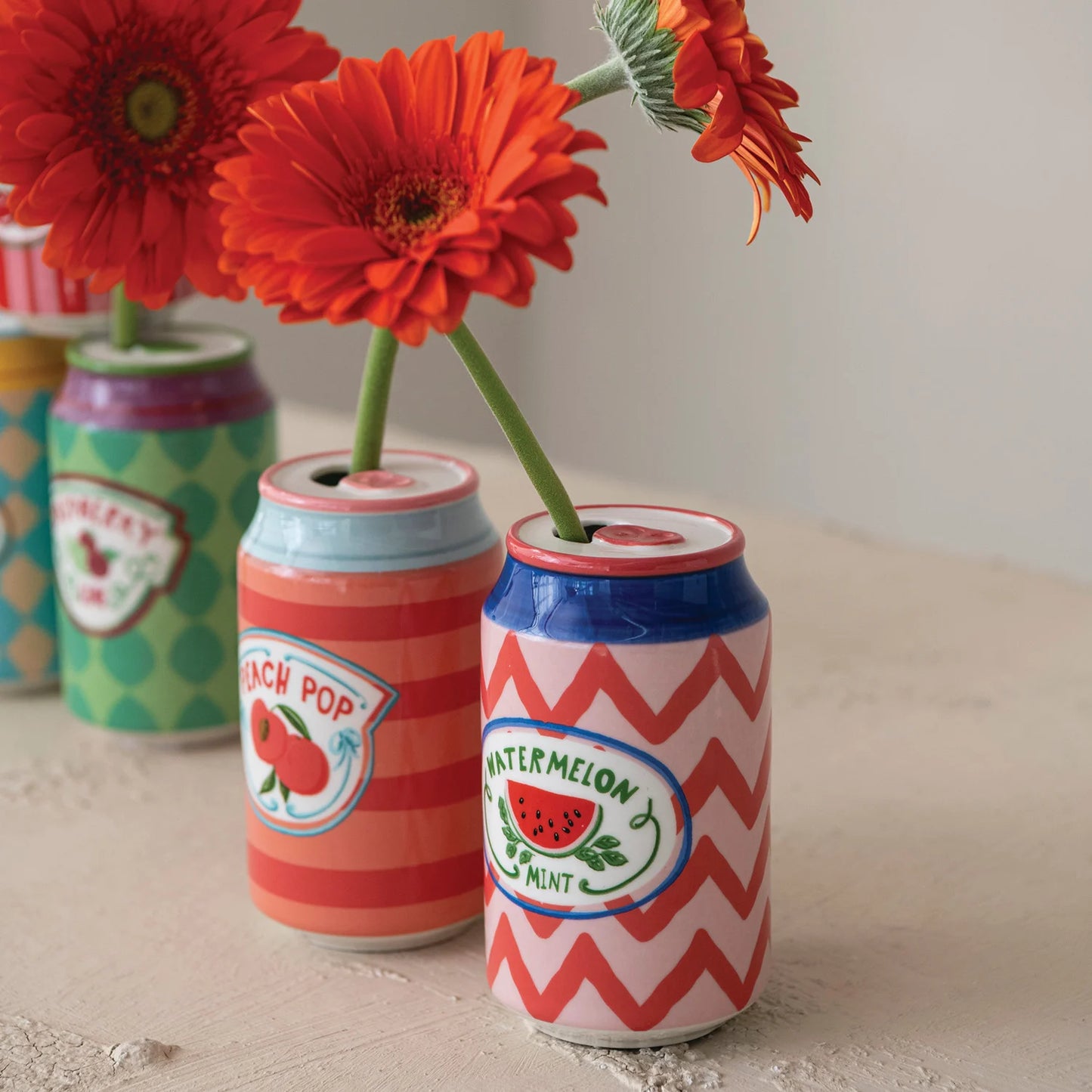 close up of ceramic soda can vases with orange flowers in them