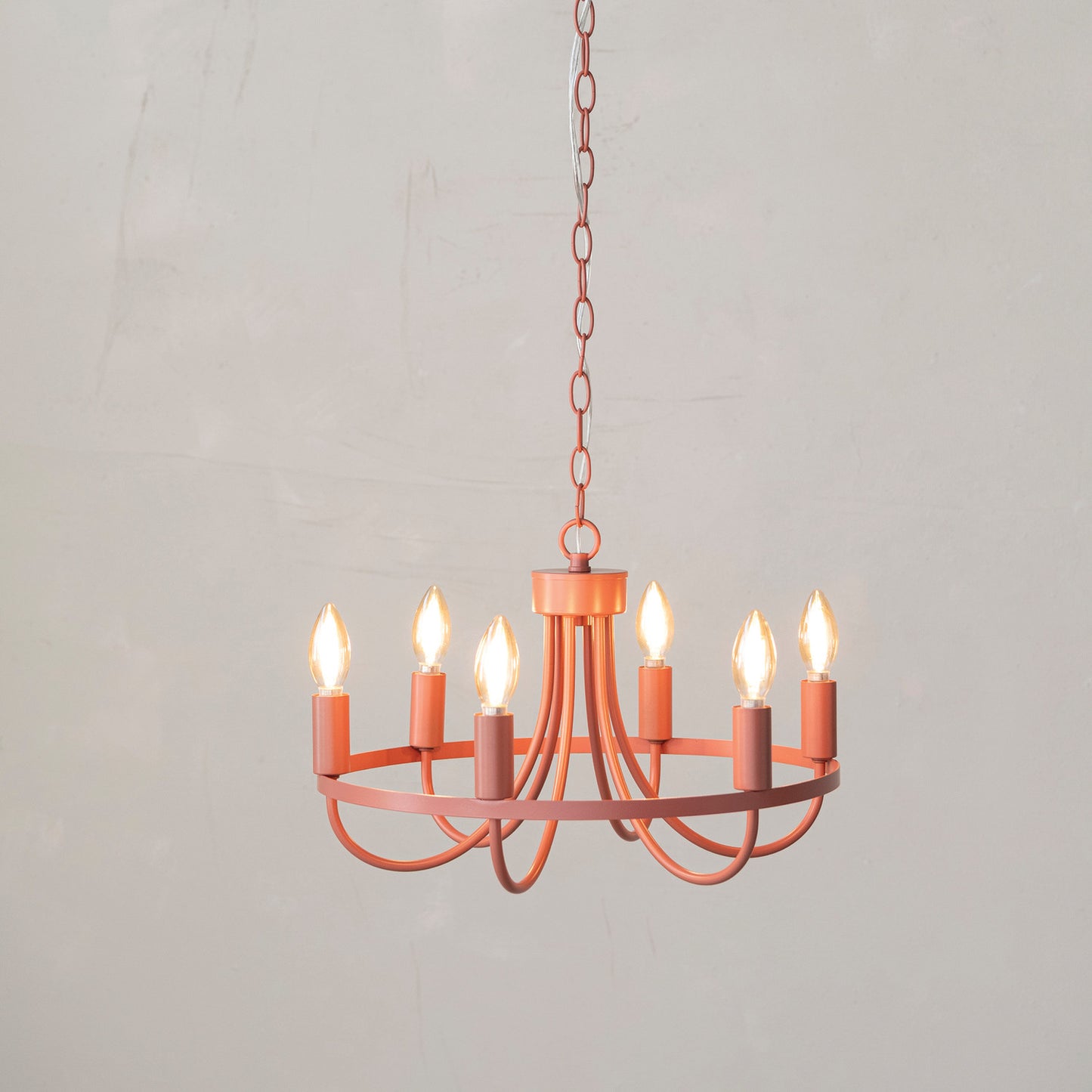 pink chandelier with the lights on hung in front of an off-white plaster wall