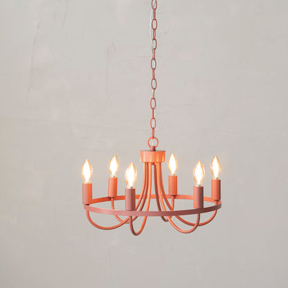 pink chandelier with the lights on hung in front of an off-white plaster wall