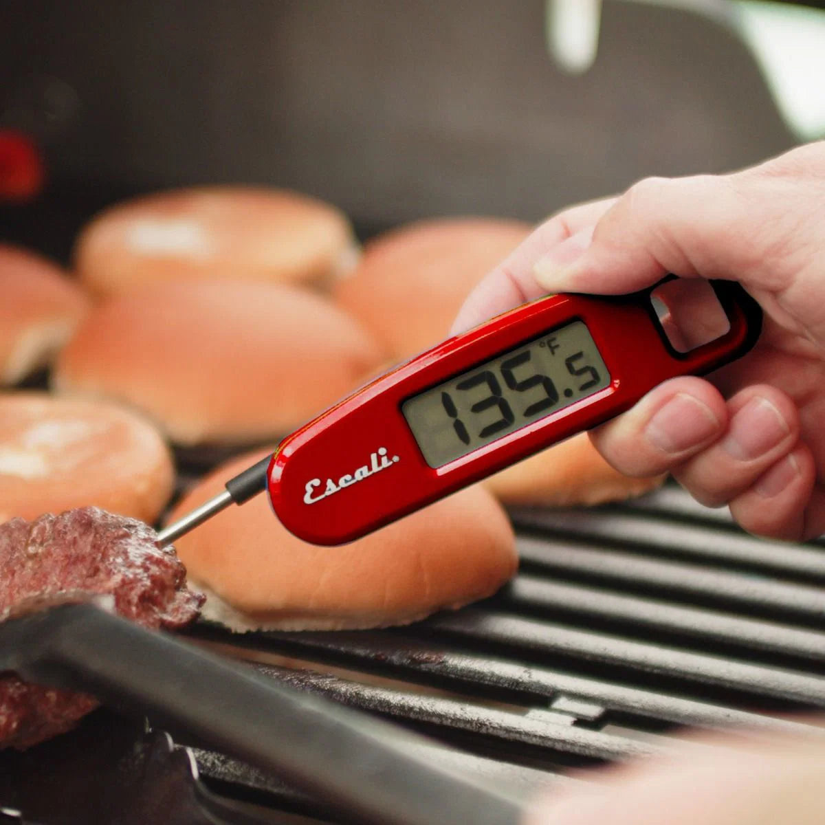 Digital thermometer reading 135.5 degrees being used on a hamburger on a grill with buns in the background