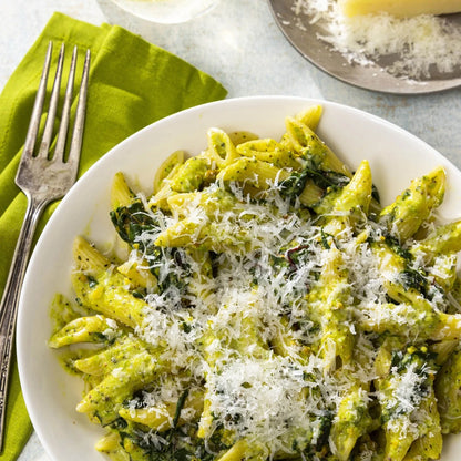 Pasta dish with spinach and parmesan cheese on a white plate with a green napkin and fork.