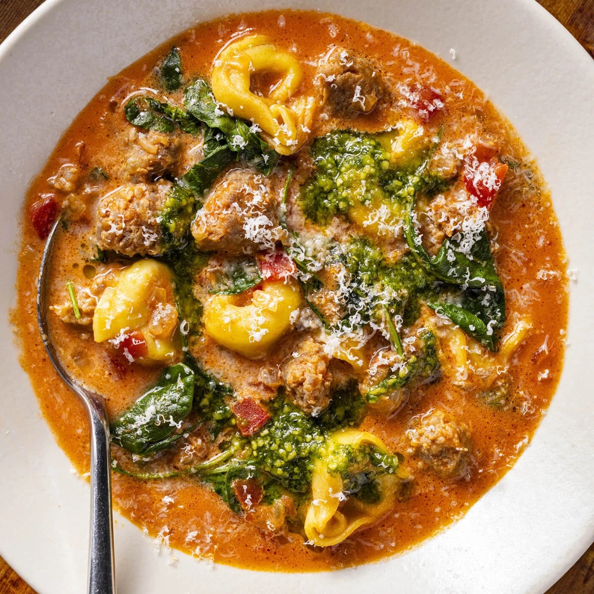 Tortellini soup with greens and meatballs in a white bowl