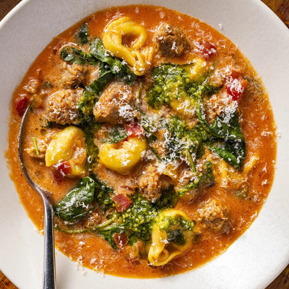 Tortellini soup with greens and meatballs in a white bowl