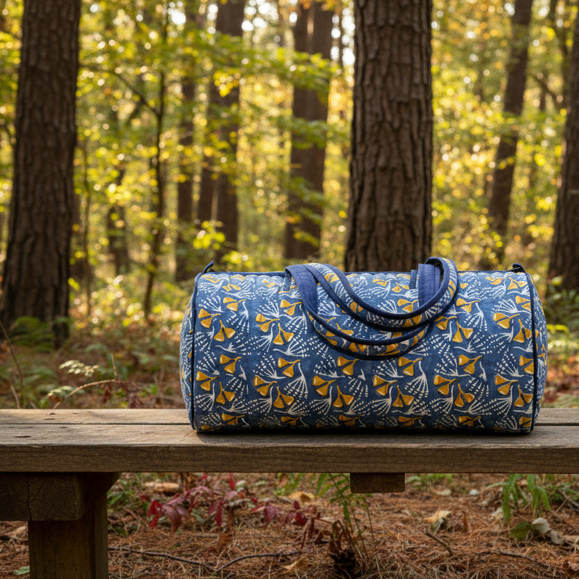 blue zip bag with yellow and white block print flowers on it set on a bench in a wooded setting
