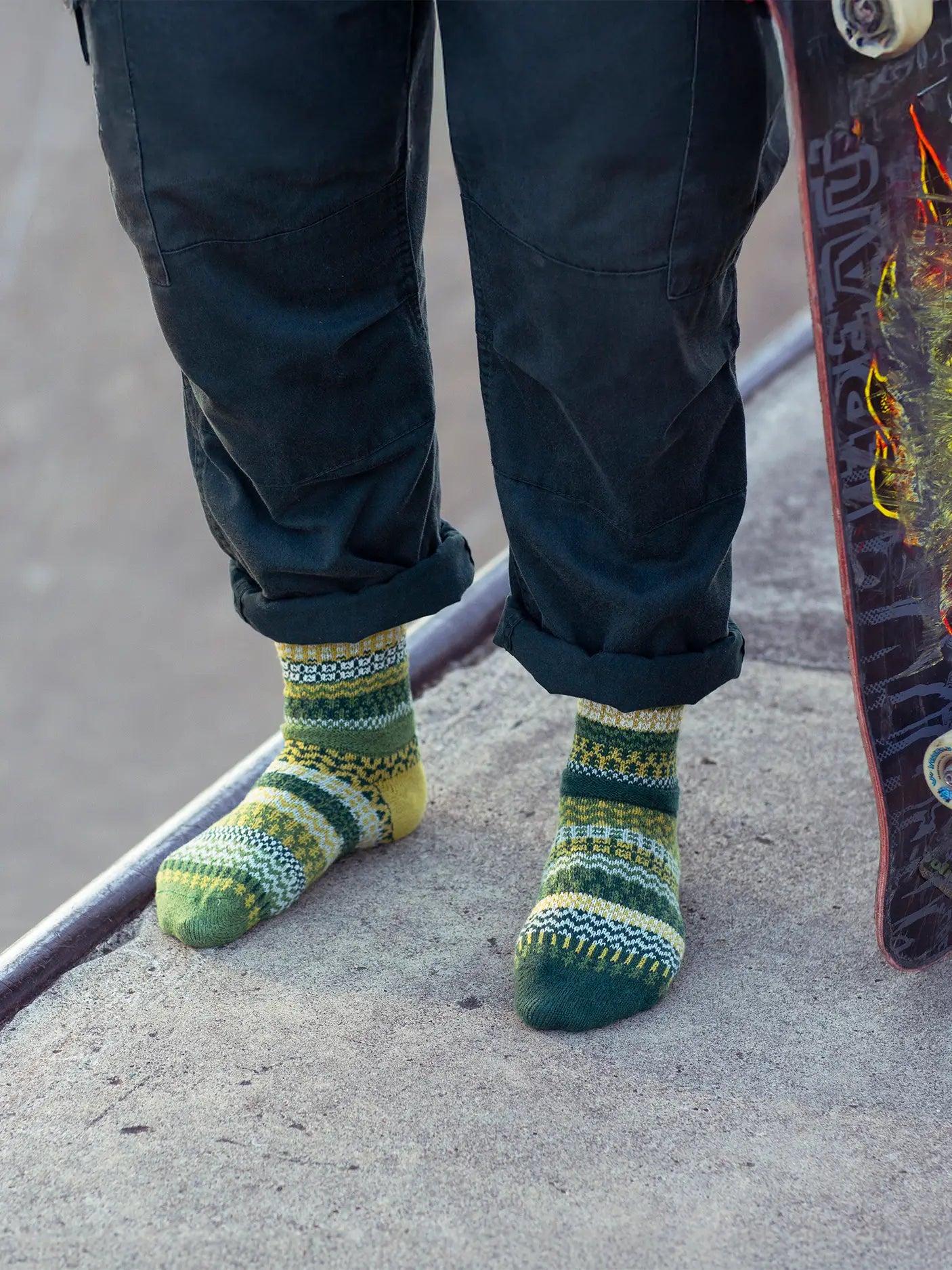 person standing on a sidewalk holding skateboard and wearing blue pants and Fiddlehead Crew Socks