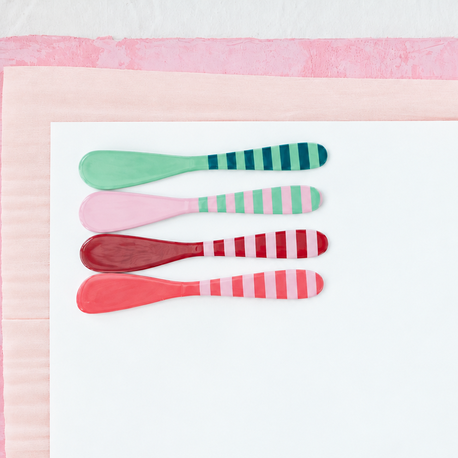4 striped metal spreaders in pink, red, and green arranged on a white and pink papers