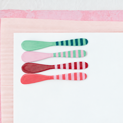 4 striped metal spreaders in pink, red, and green arranged on a white and pink papers