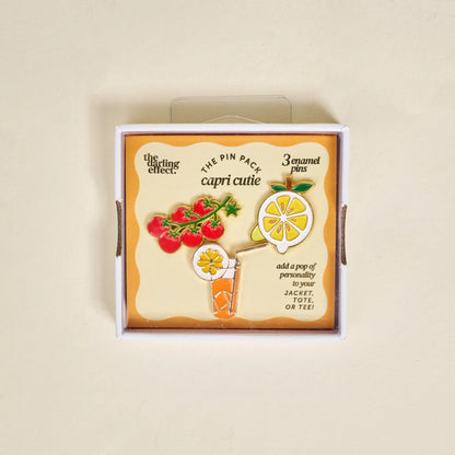 Box of enamel pins with colorful designs in box packaging on a beige background