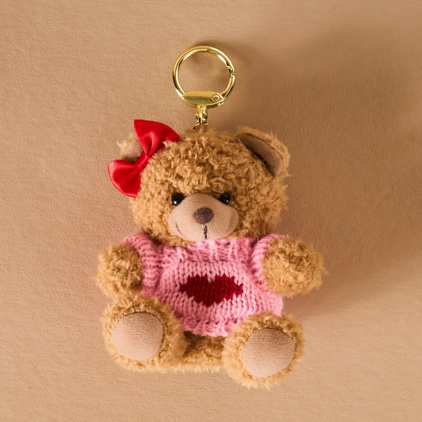 Teddy bear keychain with a pink sweater and red bow on a beige background