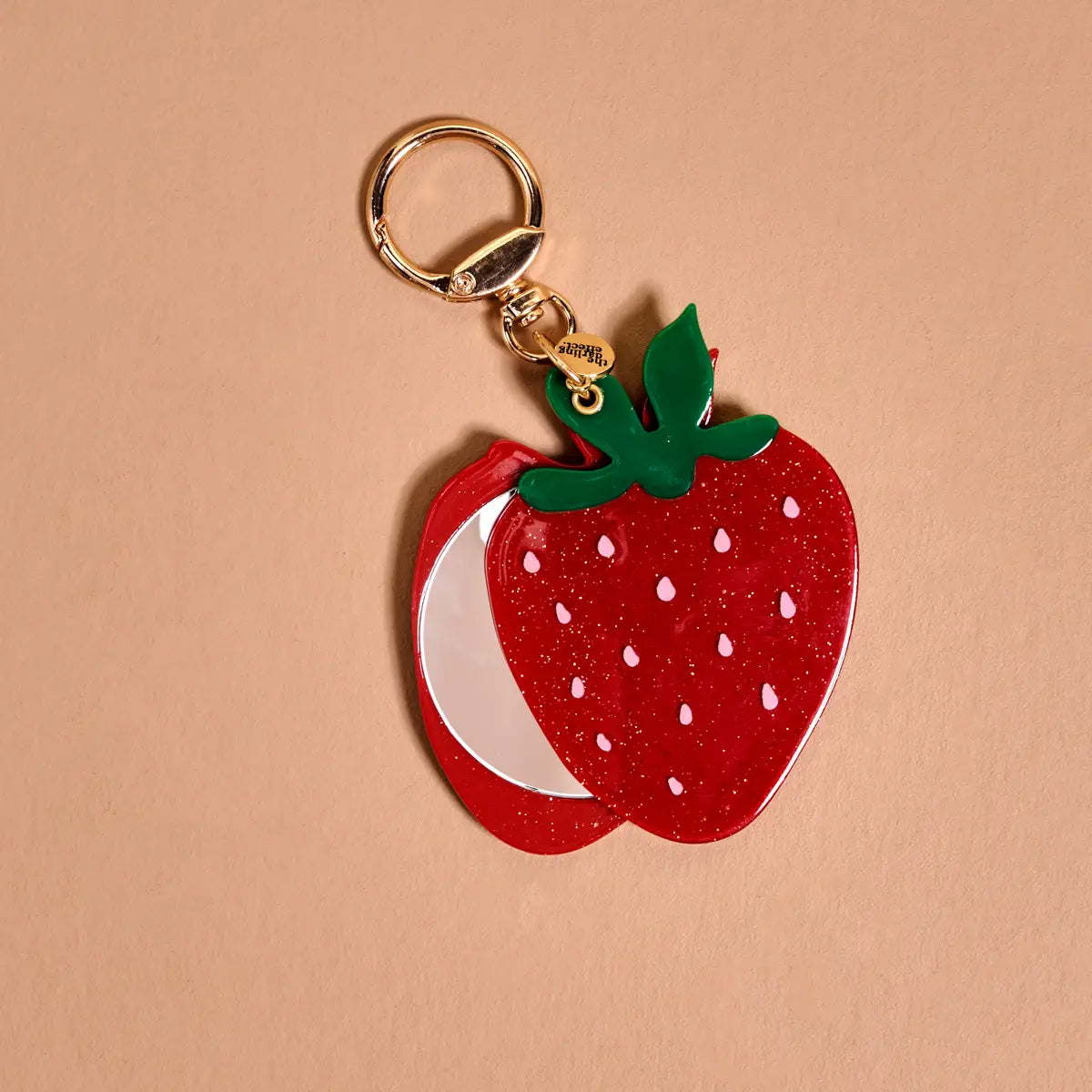 Strawberry-shaped keychain with mirror inside on a beige background