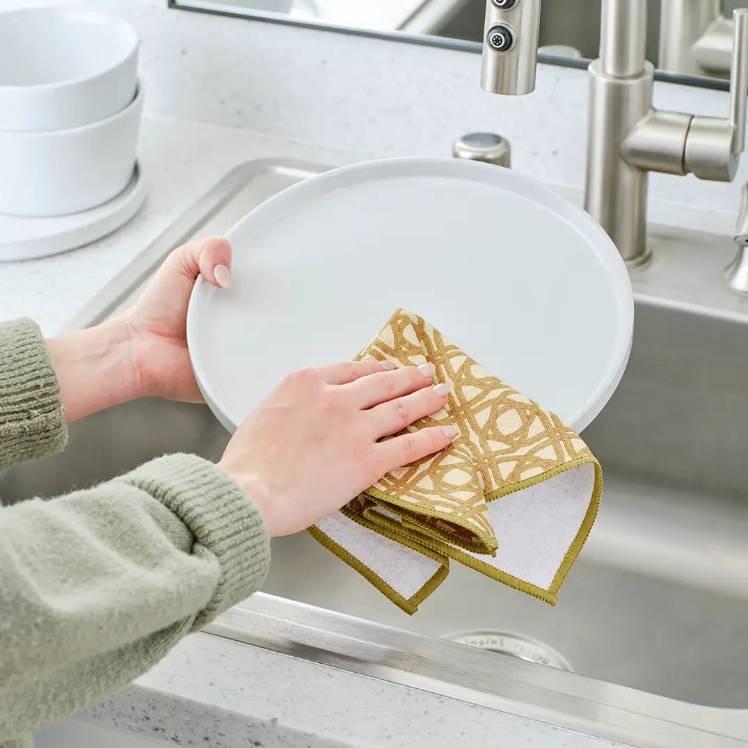 Hand using dish towel with lattice design to clean a plate over the sink.