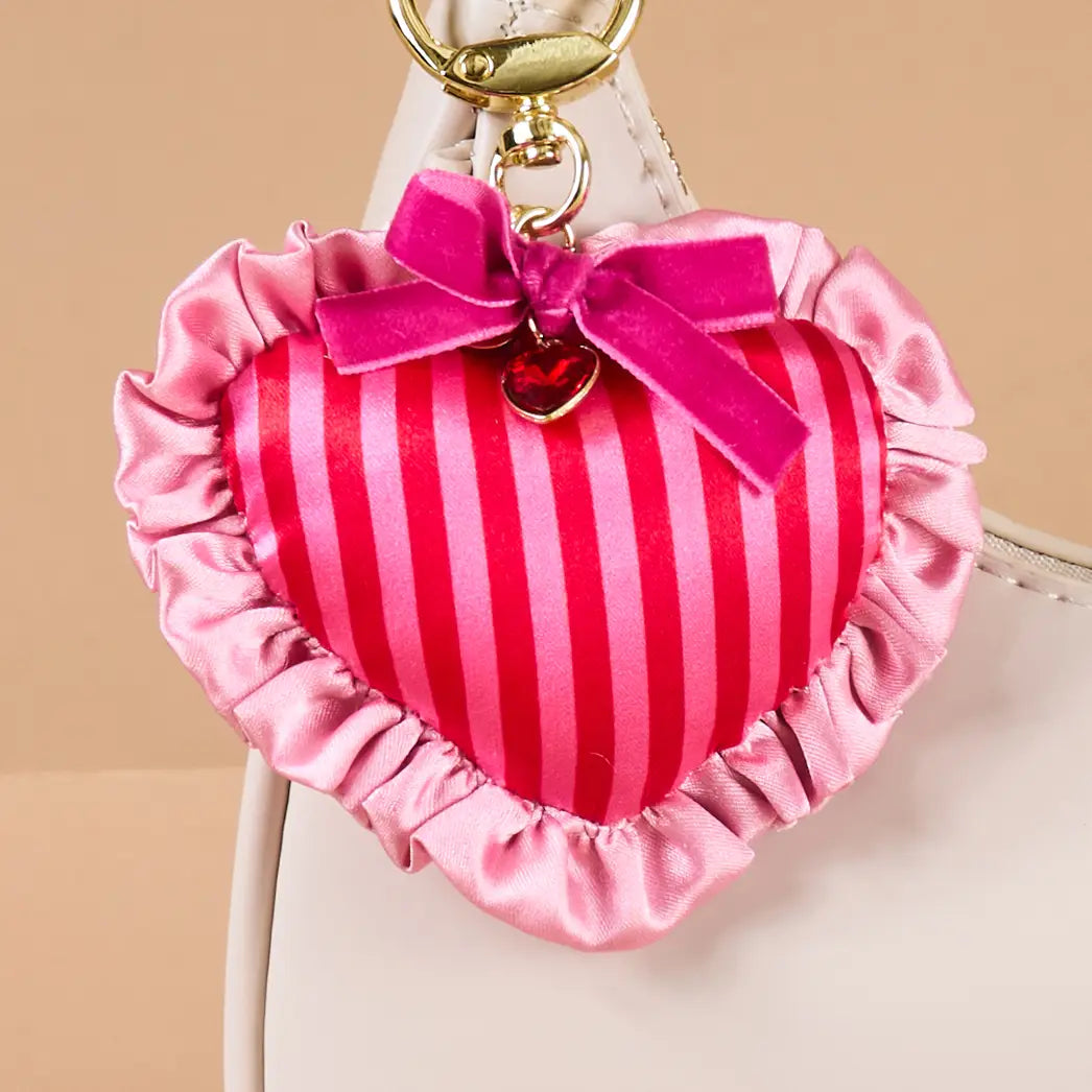 Heart-shaped bag charm with pink stripes and a bow clipped on a beige purse 
